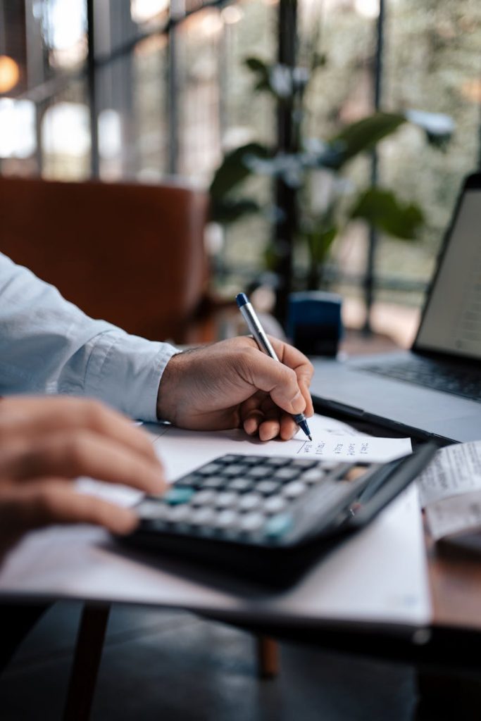 A young accountant in business attire reviews financial documents at an office desk with a laptop and calculator