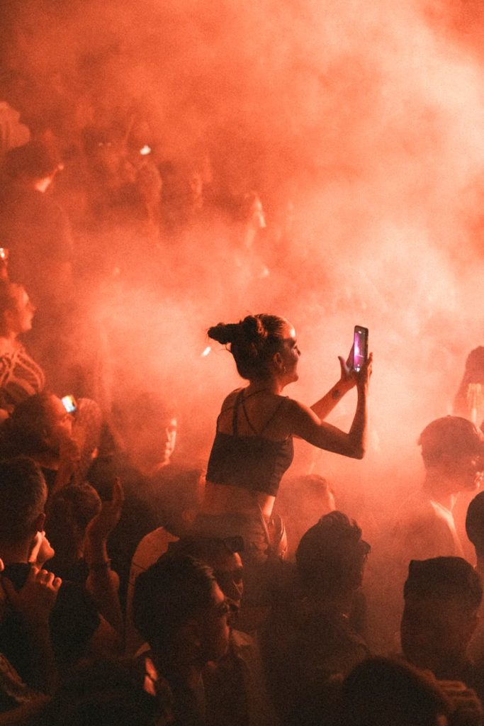 Crowded concert arena at night with a K-pop group on a lit stage and fans holding glowing light sticks