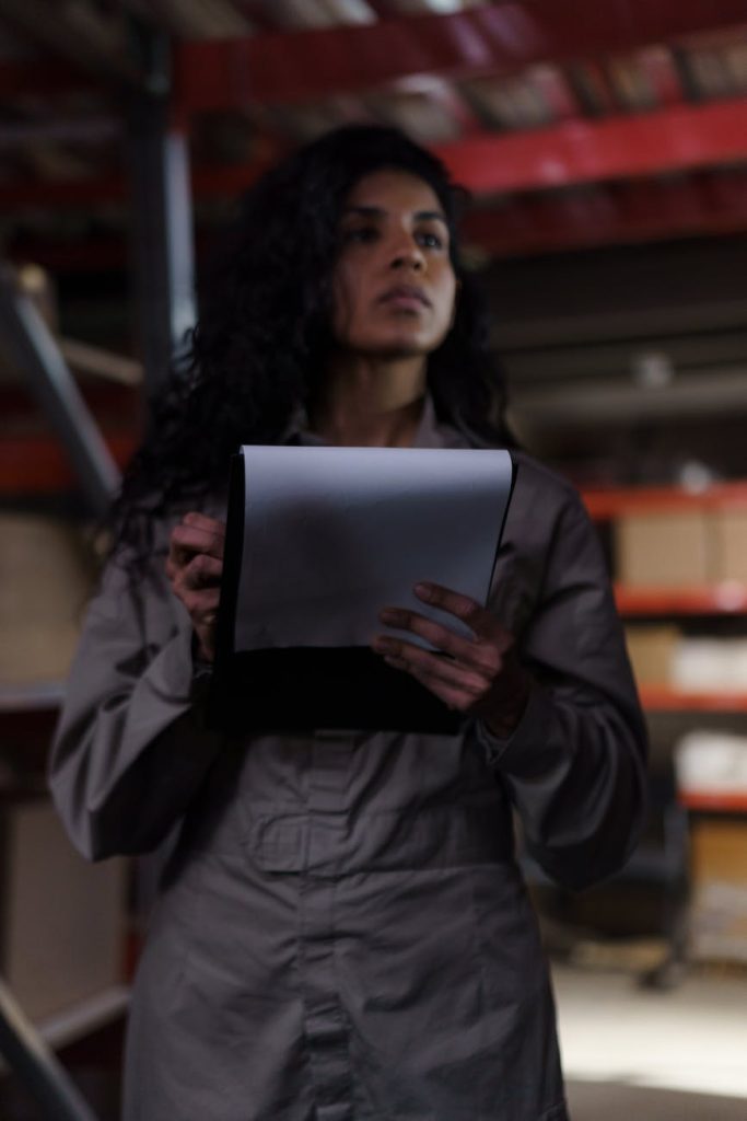 Worker checking inventory in a sparsely stocked industrial warehouse with mostly empty shelving
