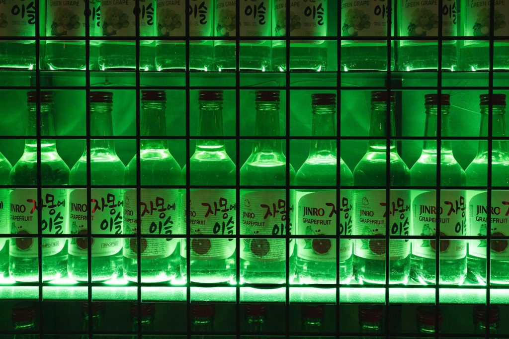 A single full glass of clear soju on a Korean restaurant table with empty chairs behind it