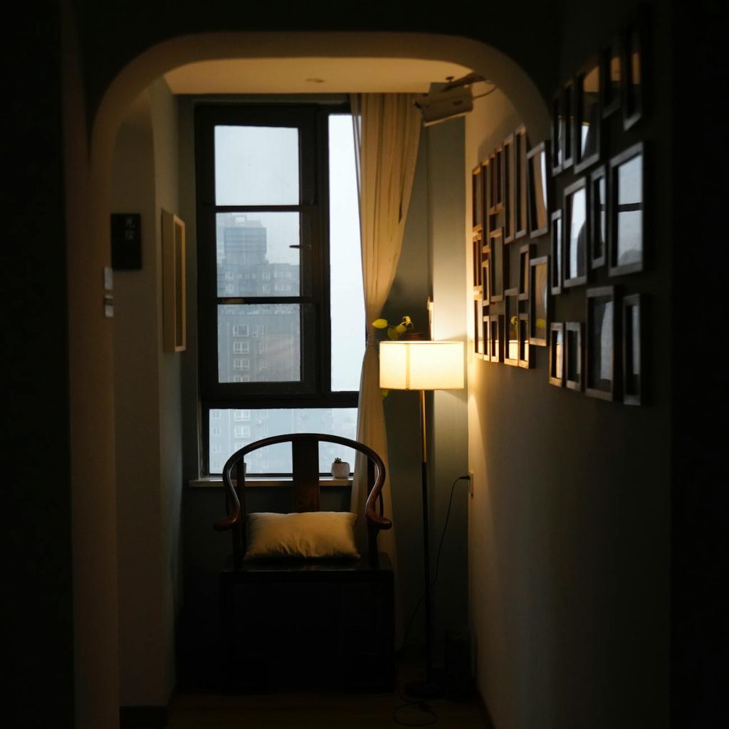 A worried young adult sits at a desk covered with bills and loan paperwork in a dimly lit room.