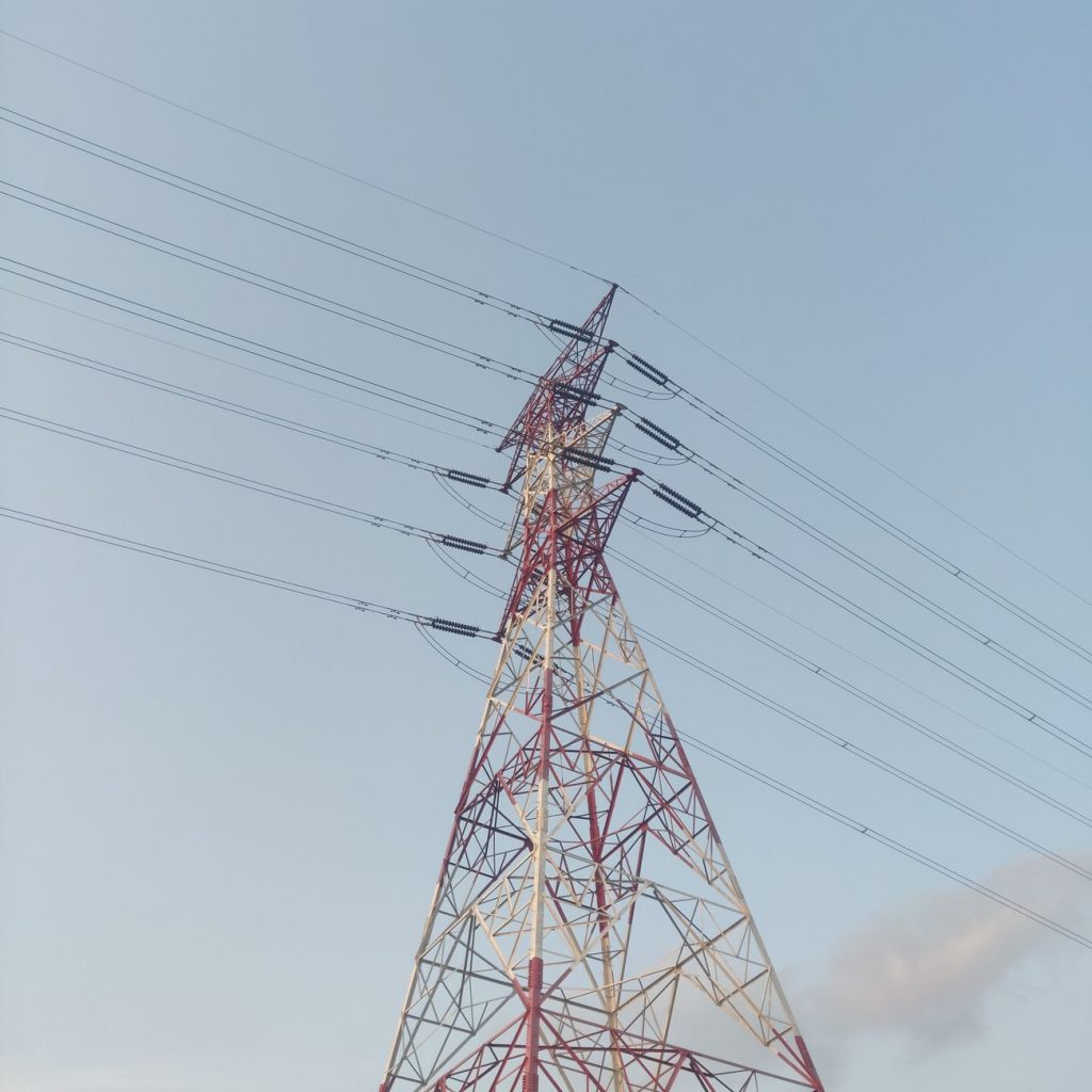 Solar panels and wind turbines beside transmission towers, with a coal power plant in the background