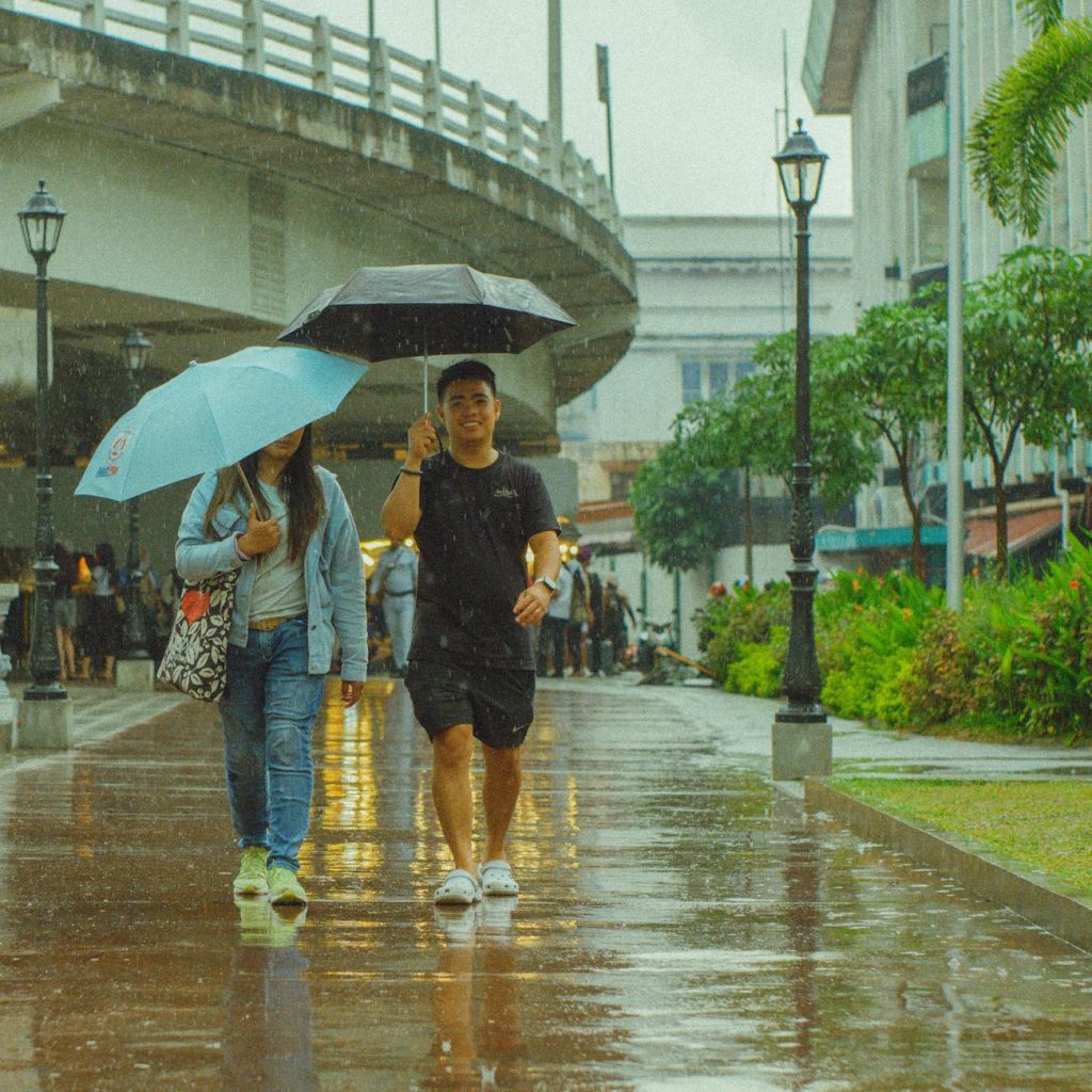 Pedestrians with umbrellas walking through heavy rain on a wet Seoul street under gray skies