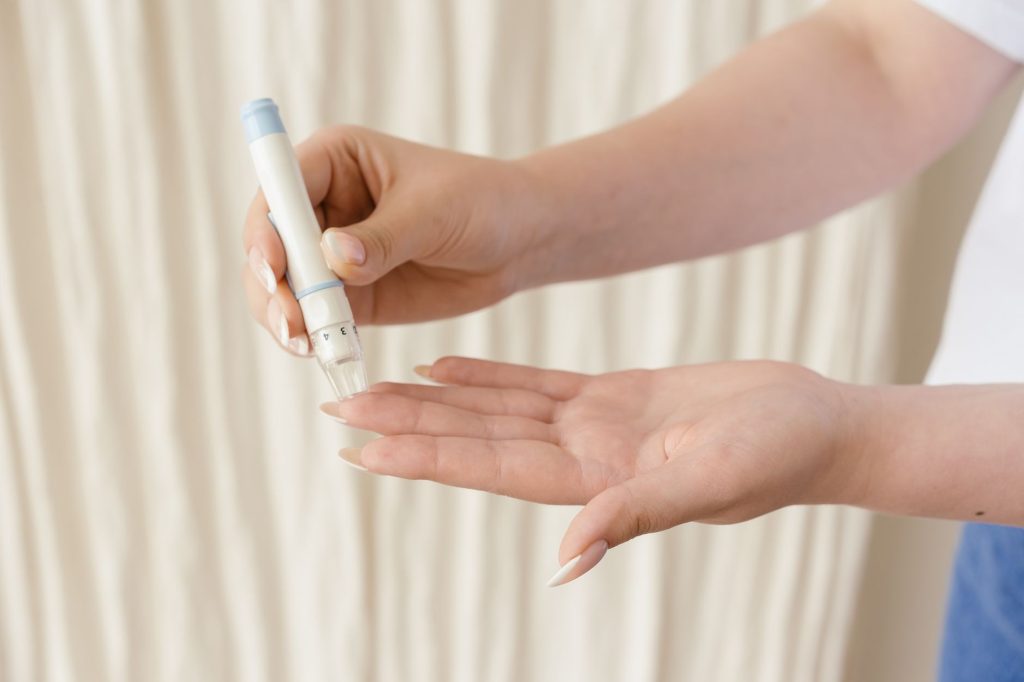 A patient at a kitchen table using a blood glucose meter with medication bottles beside them