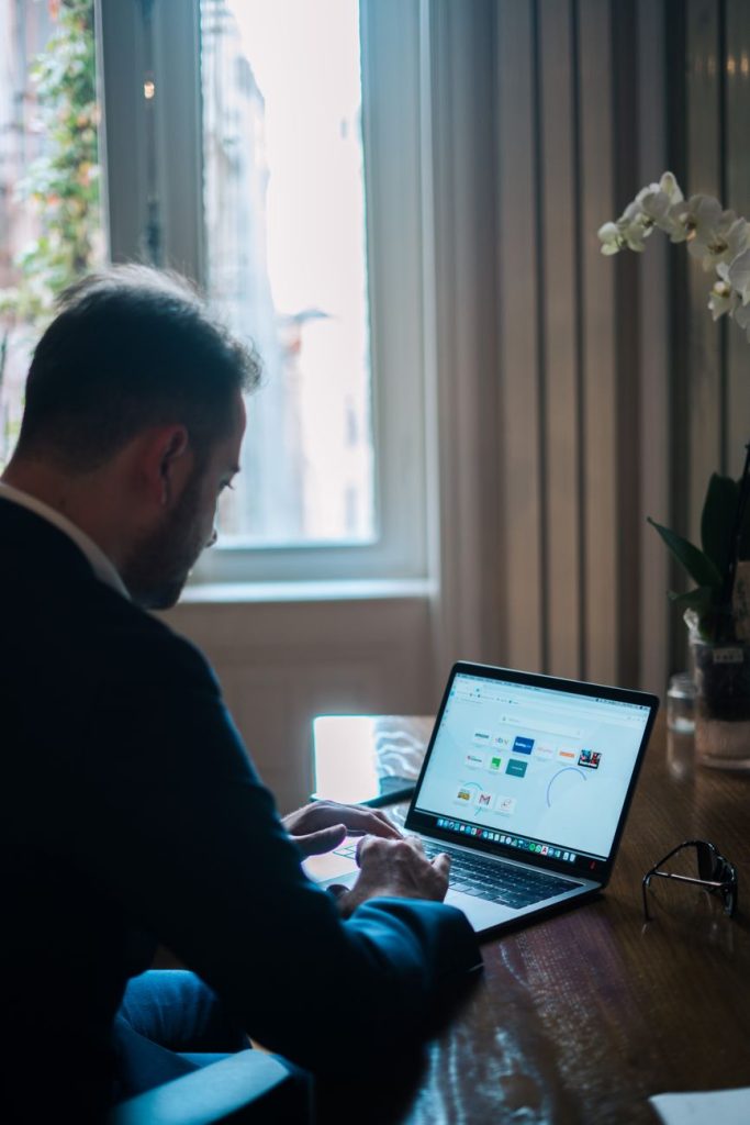 Office worker using a laptop with an AI chatbot on screen beside a wall clock in a bright office