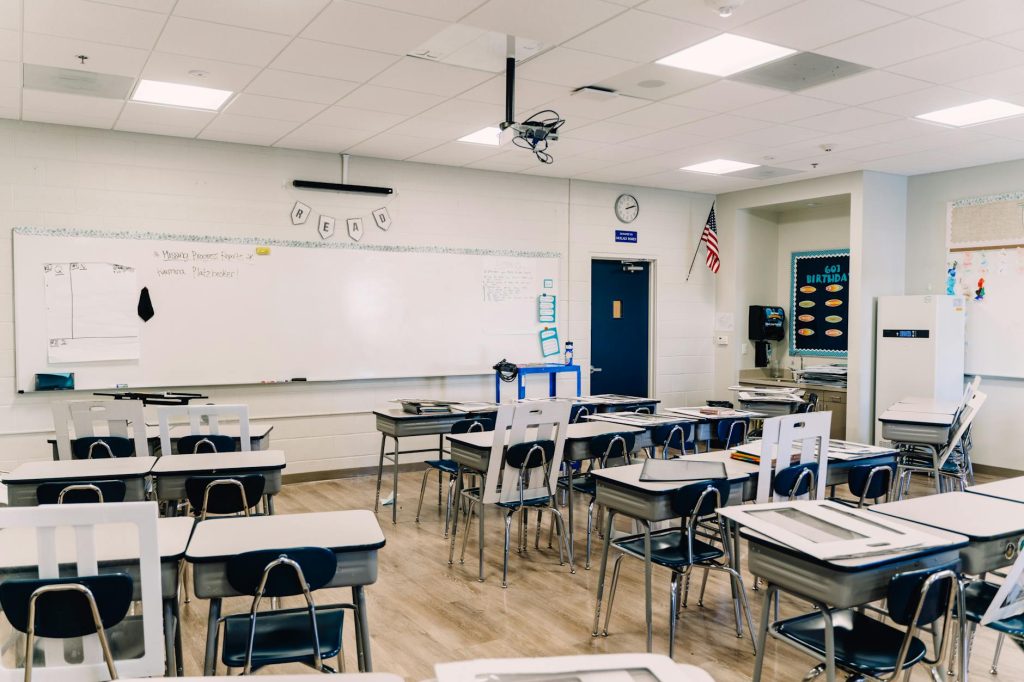 A sparsely occupied elementary school classroom with empty desks and a few seated students