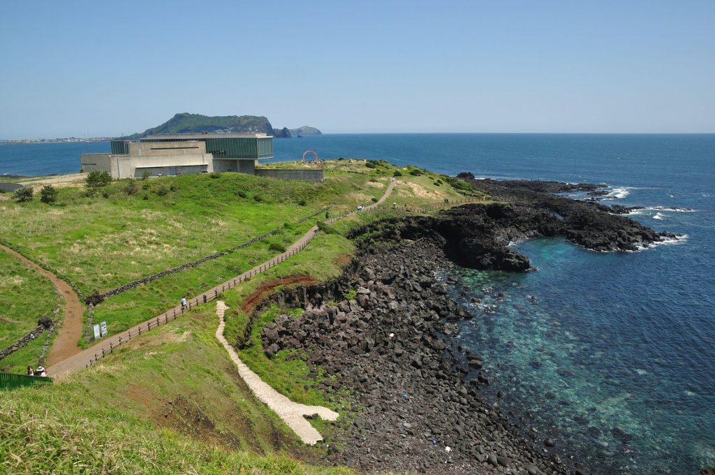 A low gray building set against a green volcanic cone on Jeju Island under a clear sky