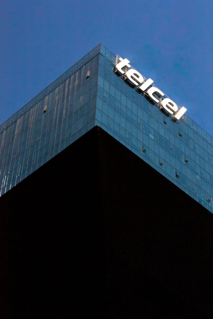 Glass tech-company headquarters at dusk with stock-ticker reflections and glowing neural-network graphics