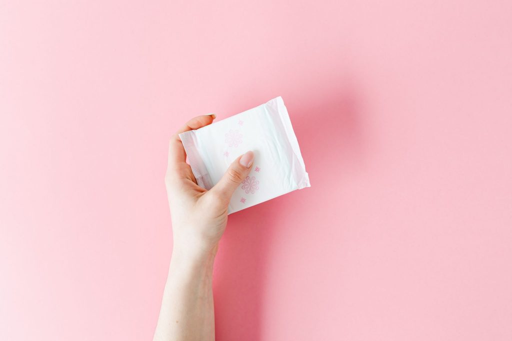 A wall-mounted free menstrual pad dispenser in a bright public facility with people nearby