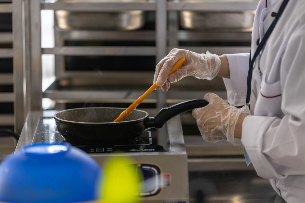 A school cafeteria worker in apron wiping sweat near hot industrial kitchen equipment