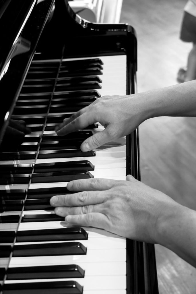 A young pianist seated at a grand piano under a warm spotlight on a darkened concert stage.