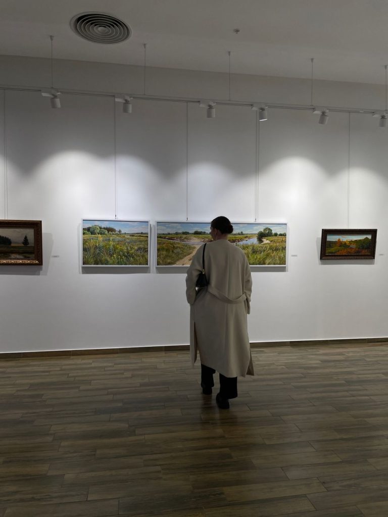 Visitors viewing large dark realist paintings hung on white walls in a modern Seoul art gallery