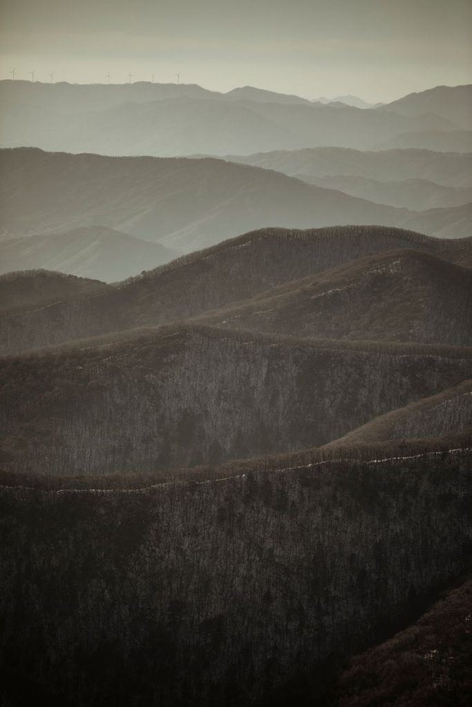 View from a mountain pass over green ridges and a small valley village with white clouds, near Mudeungsan, Korea