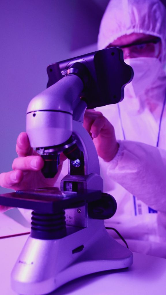 Gloved scientist uses a micropipette under a microscope to inject a single embryo cell in a lab