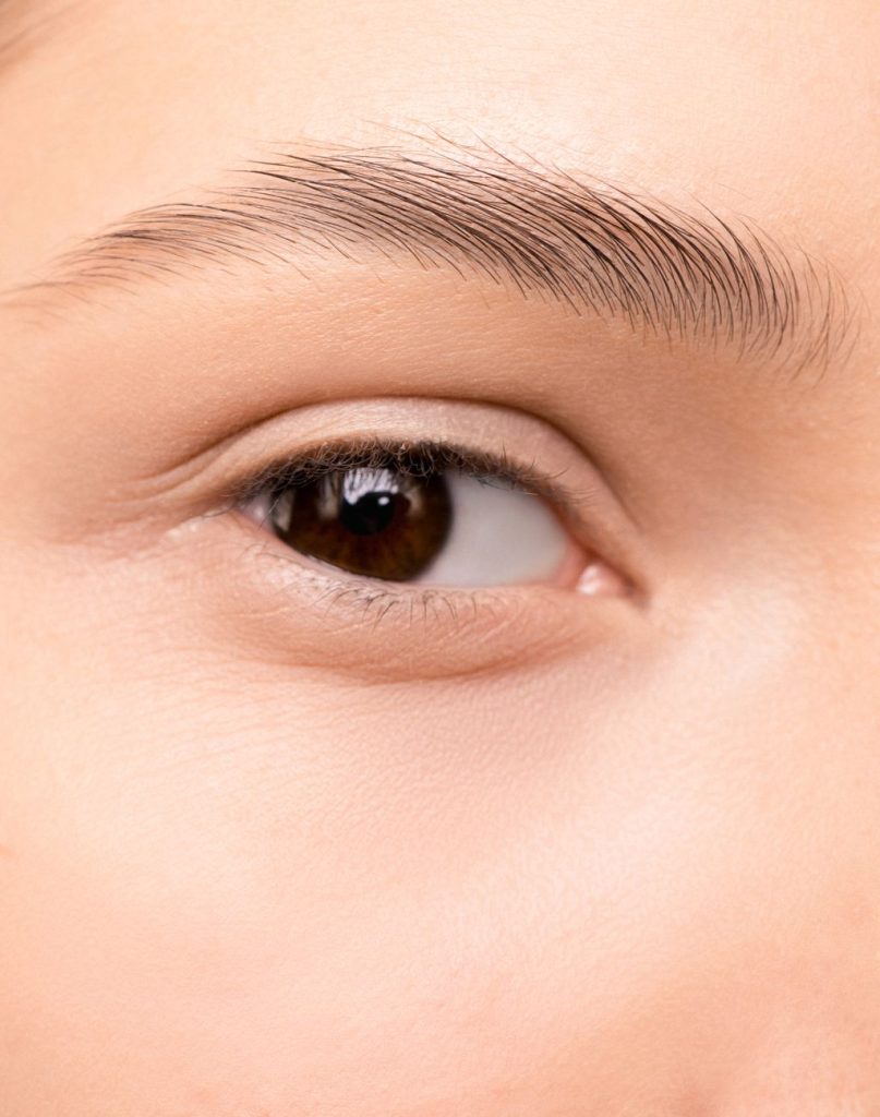 A tattooist applies semi-permanent eyebrow makeup to a client's brow in a beauty studio.