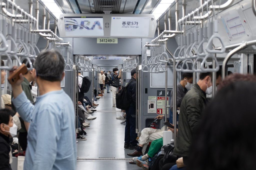 Passengers wait on a Seoul subway platform as a train arrives at a modern underground station