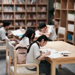 Students reading textbooks in a classroom while a teacher points at a history timeline on a whiteboard