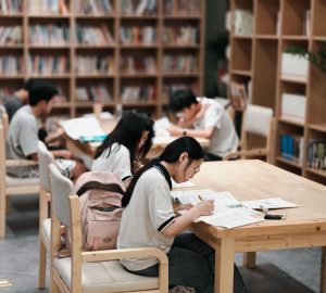 Students reading textbooks in a classroom while a teacher points at a history timeline on a whiteboard