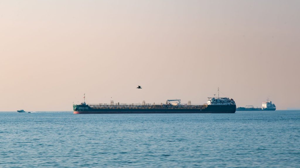 An oil tanker sailing through a narrow strait at golden hour with arid coastline in the distance