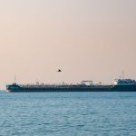 An oil tanker sailing through a narrow strait at golden hour with arid coastline in the distance