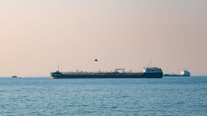 An oil tanker sailing through a narrow strait at golden hour with arid coastline in the distance